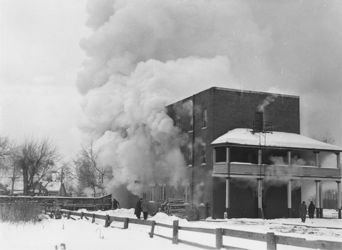 A black and white image of the Hotel Vernon, from which large clouds of smoke are billowing out of.
