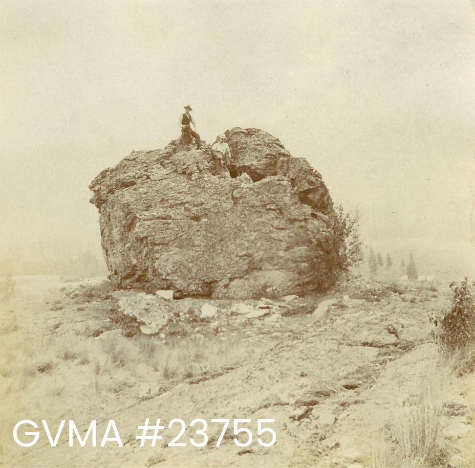 A sepia image of two men sitting on top of a very large rock.