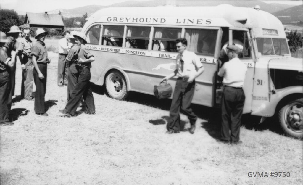 A black-and-white photo of a small bus with curtains. Several men with suitcases are standing in front of it.